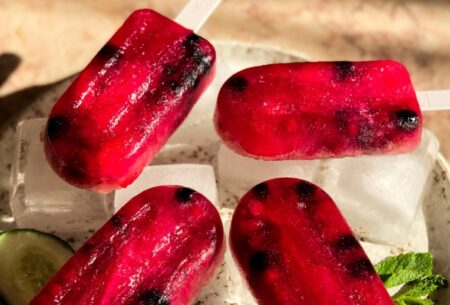 Four red fermented fizz ice lollies lying on ice cubes on a tray in the sunlight