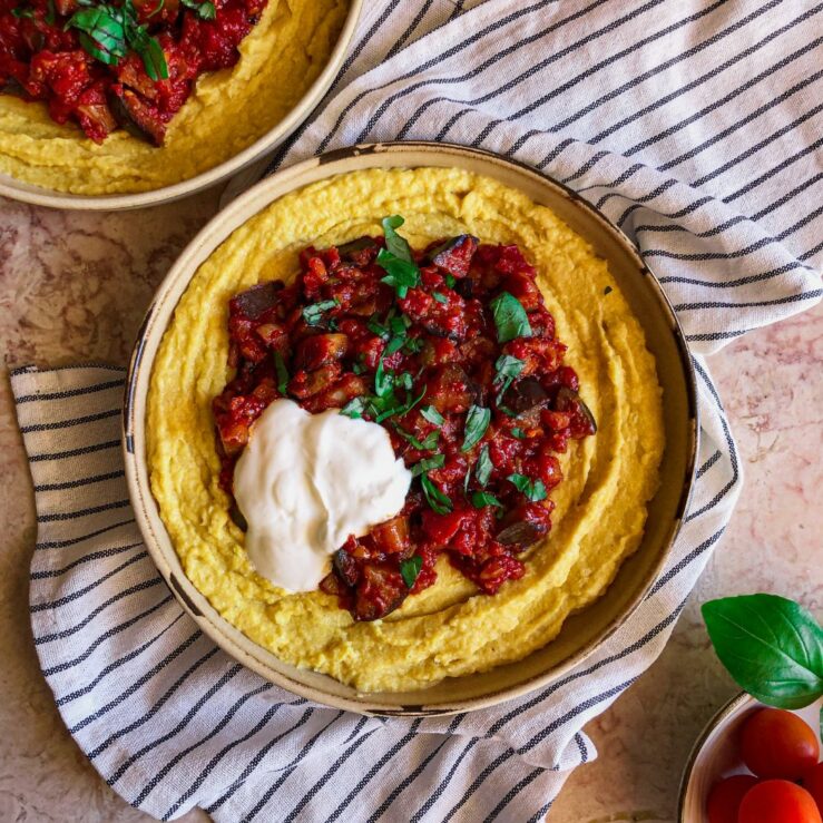 Bowl of sweetcorn polenta topped with aubergine ragu, chopped basil and a dollop of yogurt