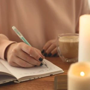 A photo of someone writing in a book with a candle lit in the foreground