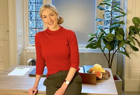 Megan Rossi sat on the edge of her desk in a red jumper